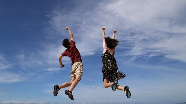 男女２人が青空の下で喜んでジャンプしている